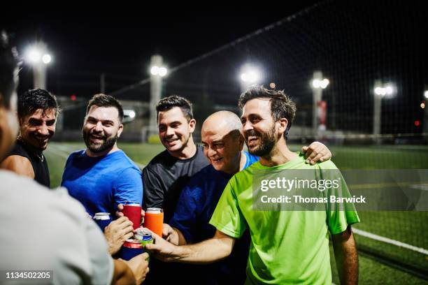 laughing male friends toasting with beers after nighttime soccer game - soccer man foto e immagini stock