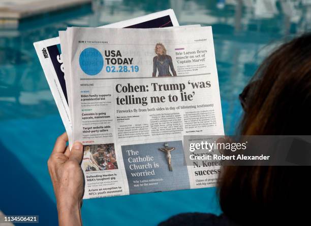 Woman relaxing beside a hotel swimming pool in Palm Springs, California, reads a copy of USA today with a headline and front page news article on...