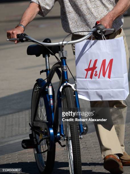 Man on a bicycle carries an H&M shopping bag as he crosses a road in Palm Springs, California.