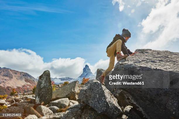 chile, cerro castillo, boy climbing on rock in mountainscape - boy rock climbing stock-fotos und bilder