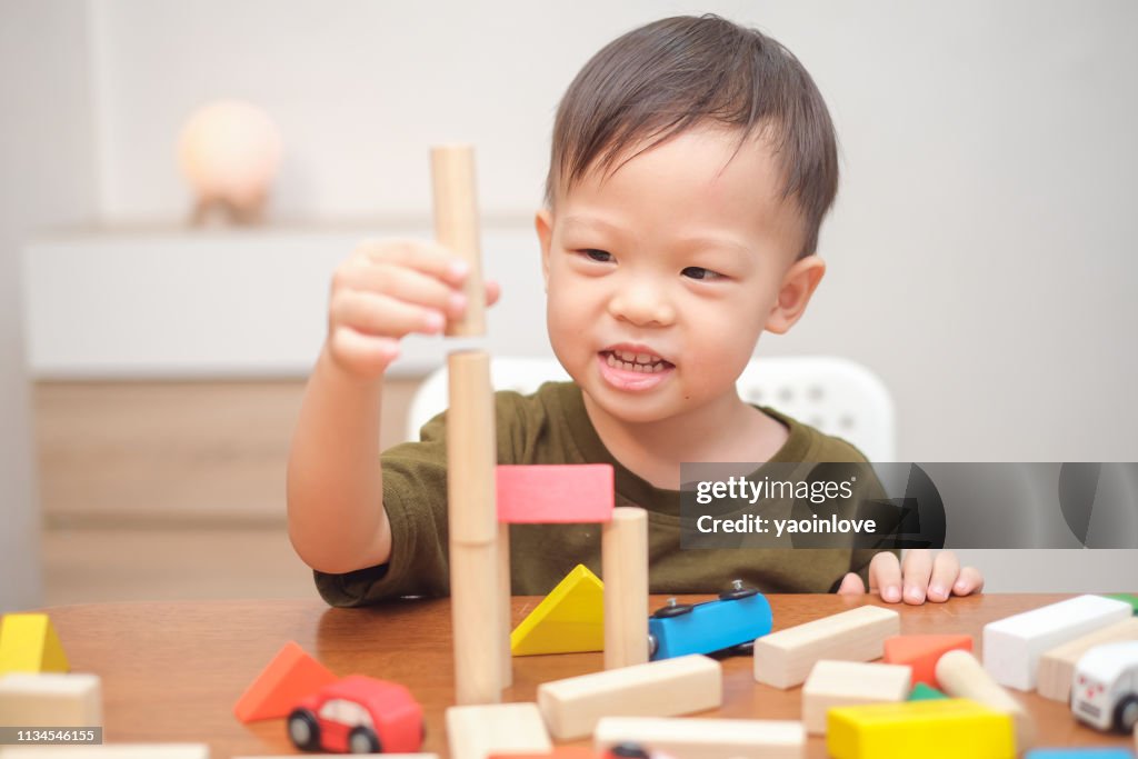 Cute little Asian 2 - 3 years old toddler boy child having fun playing with wooden building block toys indoor