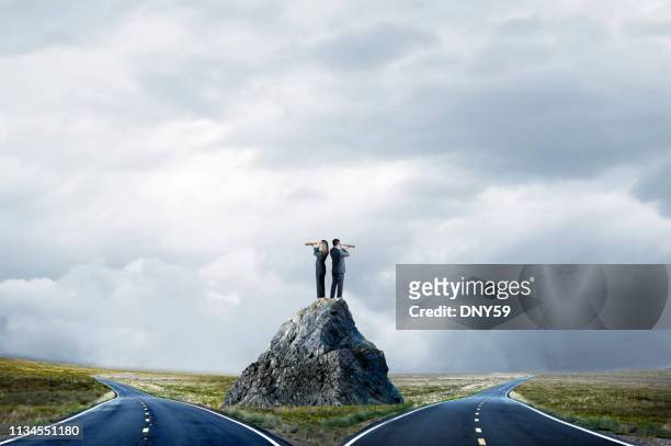 business people standing on large rock looking at fork in the road - fork in the road stock-fotos und bilder