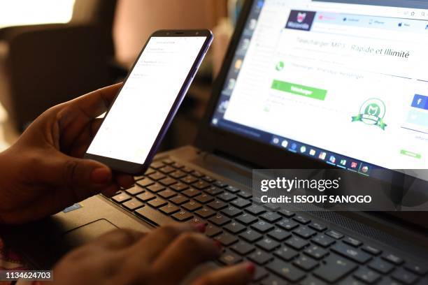 Woman uses a smartphone in front of a laptop on April 3 in Abidjan. - According to the figures of the platform of the fight against cybercrime of the...