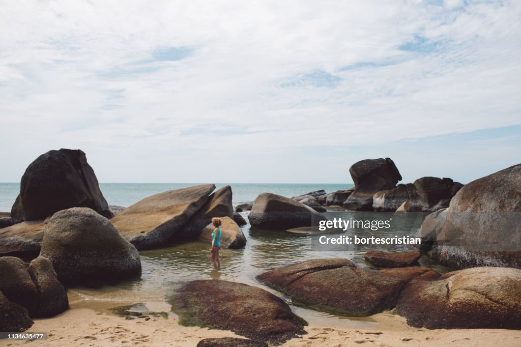 Woman Standing In Sea By Rocks Against Sky