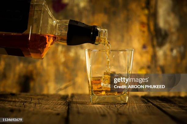 barman pouring whiskey in front of whiskey glass and bottles on black table with whiskey and ice on a glass table - spiritueux photos et images de collection