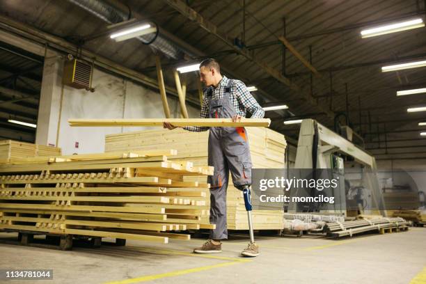 jonge timmerman met prothese been op het werk dragen houten plank - amputatie stockfoto's en -beelden