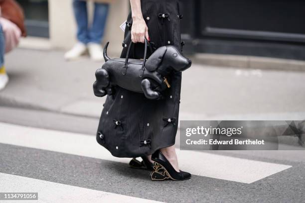 Guest wears a lustrous black watered skirt with bejewelled small bows, a black dog shaped handbag, black pumps with fantasy heels representing a...