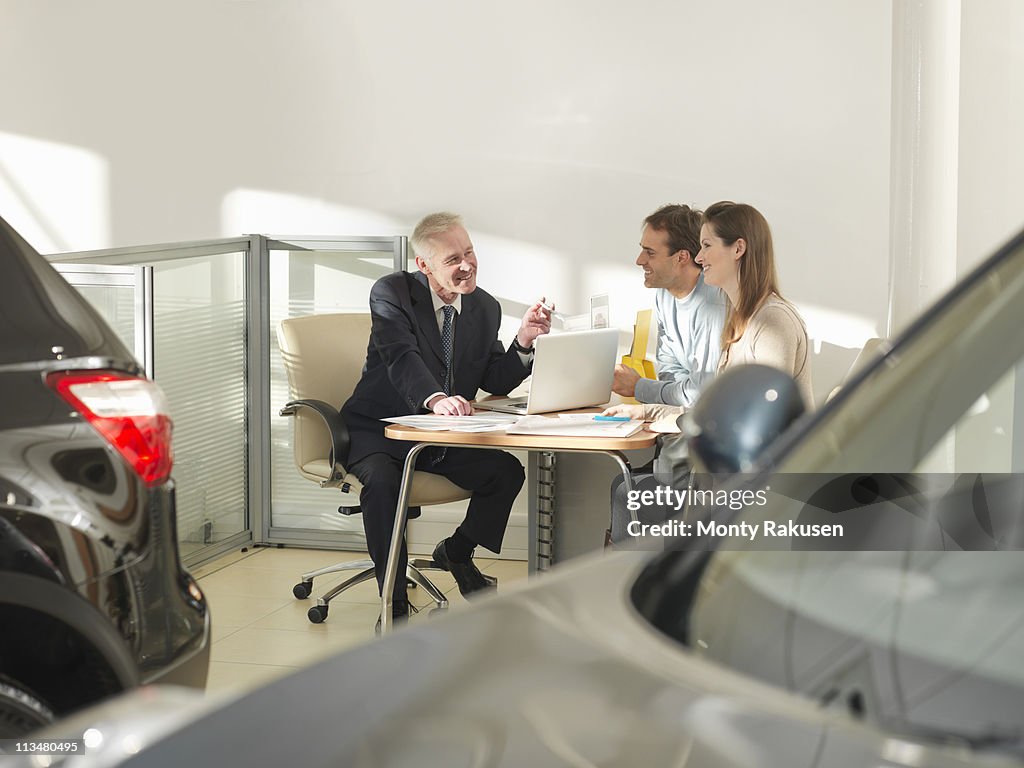 Salesman with laptop in car showroom talking with male and female customers