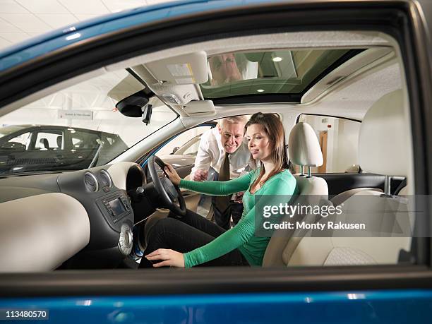 salesman advises female customer who is sat in car in car dealership - car dealership test drive stock pictures, royalty-free photos & images