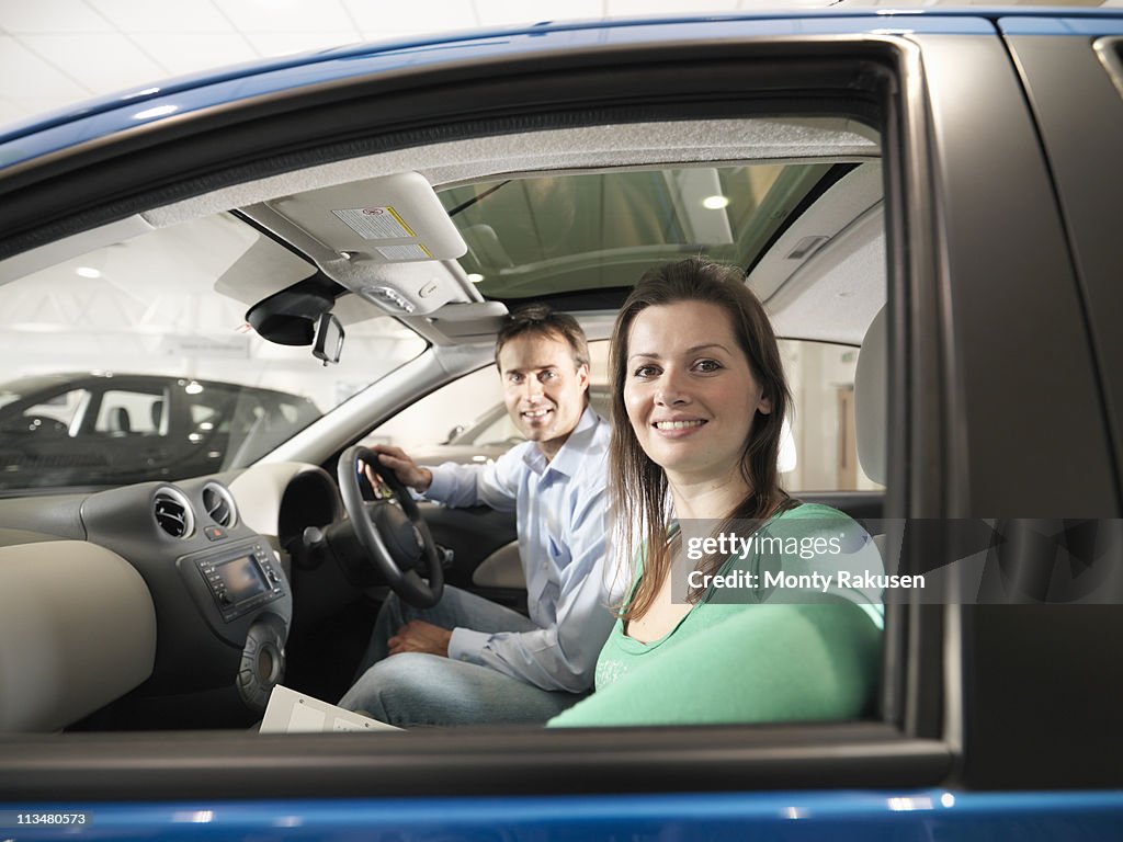 Customers looking to camera sitting in front seats of a car in car dealership