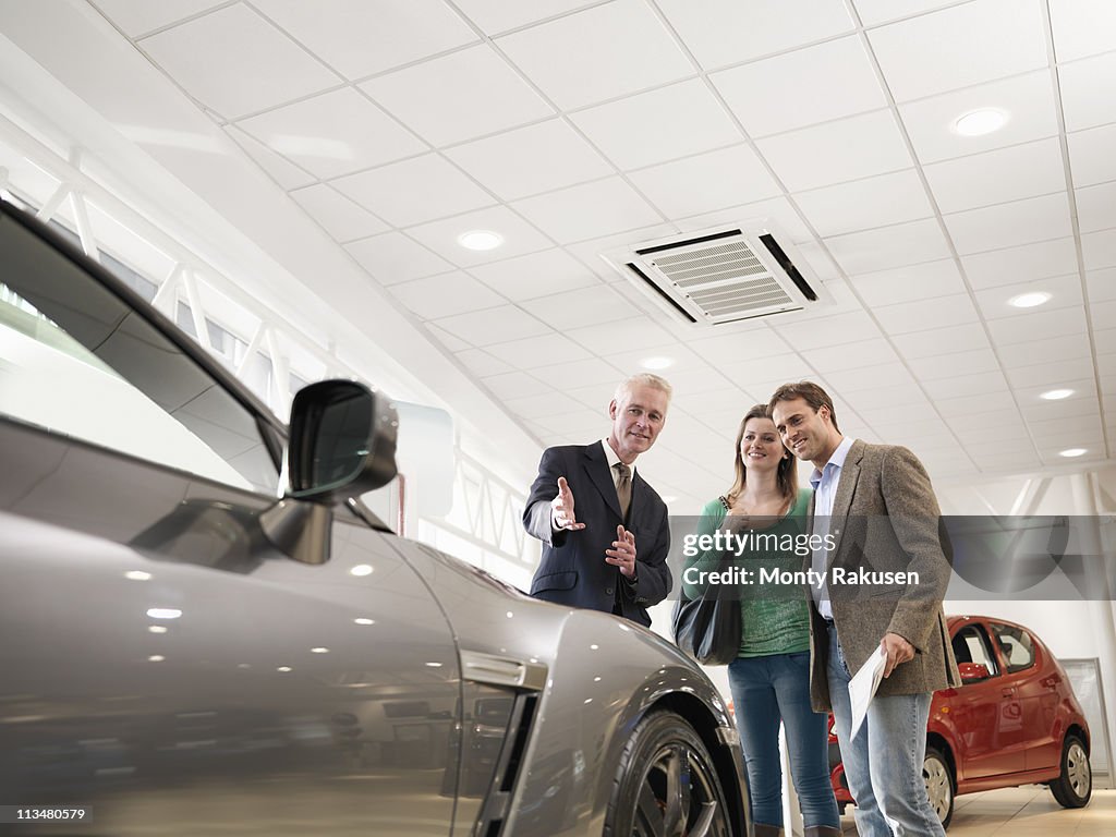 Salesman shows customers car in car dealership