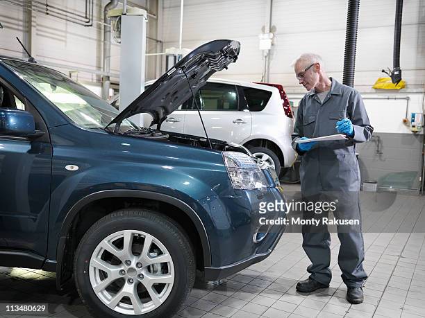 mechanic in car dealership workshop standing by car, with open bonnet, holding pen and paper, analyzing engine - hood clothing stock pictures, royalty-free photos & images