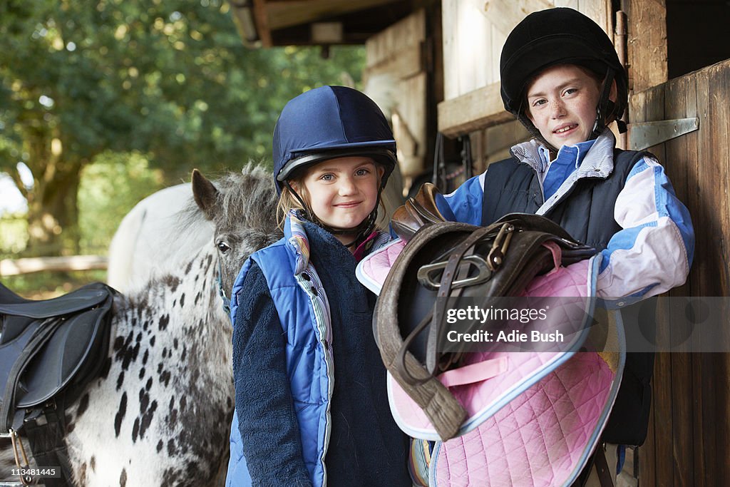 Two girls holding saddles with pony