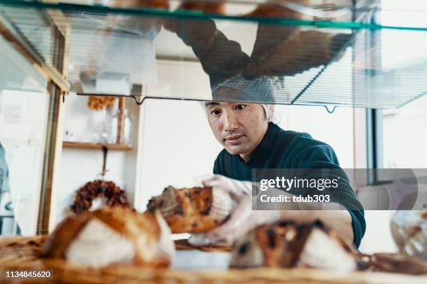 mitteler erwachsener mann, der brot in seiner kleinen bäckerei stellt - bakery display stock-fotos und bilder