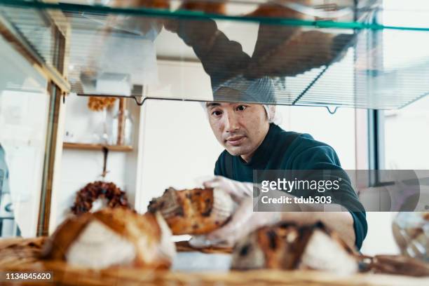 半ば大人の男性は彼の小さなビジネスベーカリーでの表示にパンを入れて - eastern ストックフォトと画像