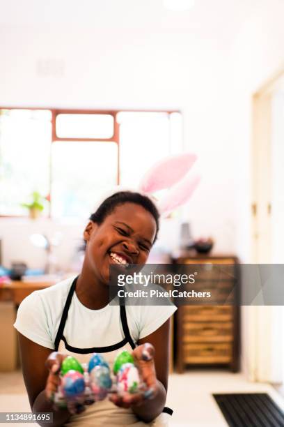 glückliches junges afrikanisches mädchen, das ihre handbemalten ostereier vor die kamera zeigt - african family easter stock-fotos und bilder