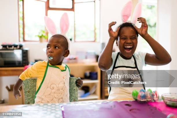 junge mädchen lacht, wie junge legt ganze ostereier in den mund - african family easter stock-fotos und bilder