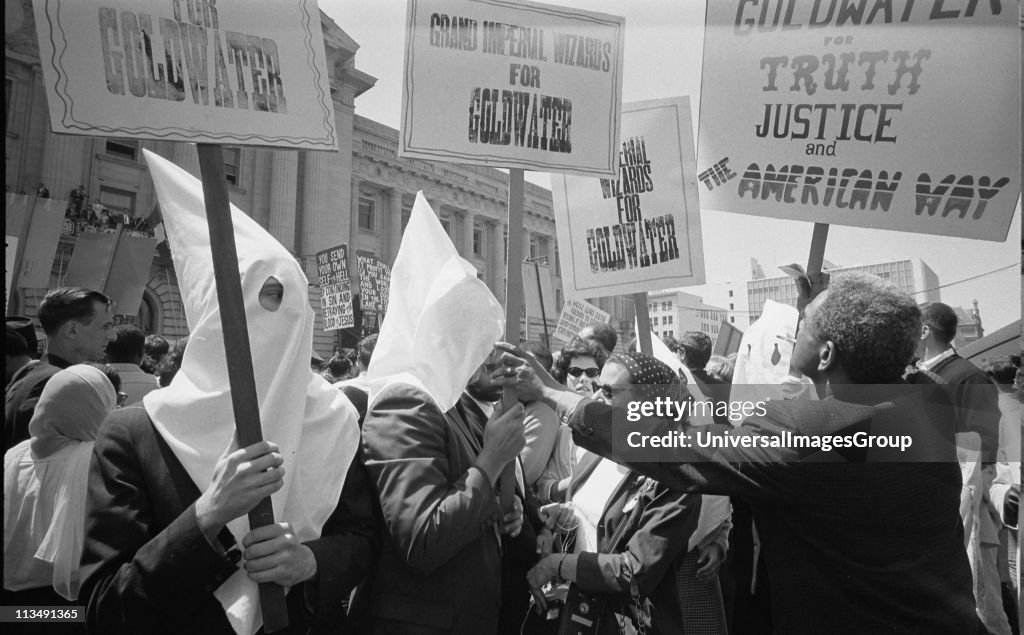 Ku Klux Klan members supporting Barry Goldwater's campaign for the presidential nomination at the Republican National Convention, San Francisco, California, as an African American man pushes signs back: 12 July 1964. Photographer: Warren K Leffler.