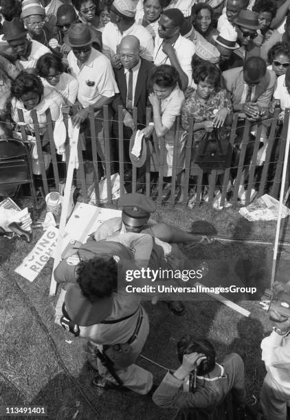 Civil rights march on Washington, D.C. Photograph shows a crowd of African Americans behind a storm fence with police carrying a woman on the other...