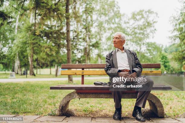 senior man zittend op een bankje in het park - zitbank stockfoto's en -beelden