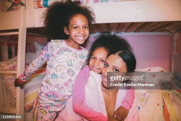 Afrolatina Twin Daughter embracing Afrolatina Mom from behind. Second daughter smiling and holding onto bunk bed staircase.