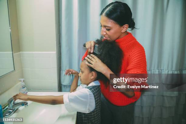 afrolatina mom with afrolatina daughter in the bathroom. mom is combing daughter's afro. daughter reaches out for faucet handle. - the bronx foto e immagini stock