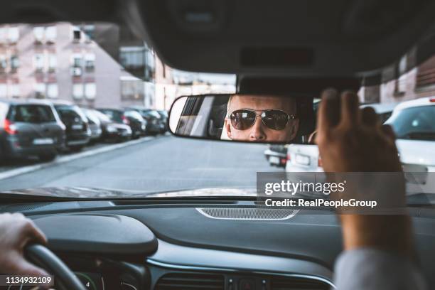 zuversichtlicher mann sitzt im auto und stellt rückspiegel ein - rückspiegel stock-fotos und bilder