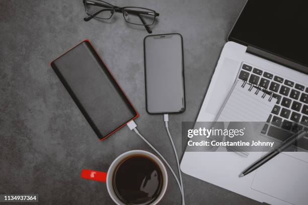 laptop, mobile phone charging with power bank and coffee mug on work desk - phone accessory stock pictures, royalty-free photos & images