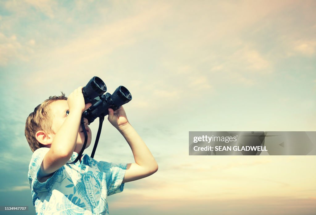 Boy looking through binoculars at sky