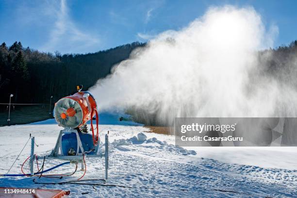 snow machine blowing artificial snow over a ski slope on a sunny day - canon stock pictures, royalty-free photos & images