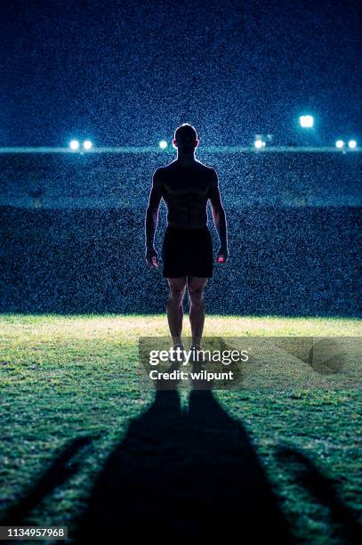 silhouette of strong male athlete standing in front of stadium in the rain at night - football player silhouette stock pictures, royalty-free photos & images