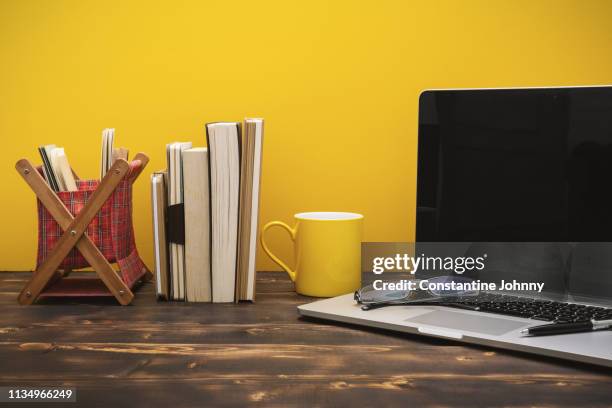 laptop and books in a row on wooden desk against yellow background - johnny stark stock pictures, royalty-free photos & images