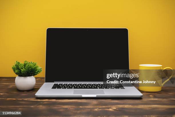 laptop and yellow coffee mug on office desk against yellow background - büro tisch leer stock-fotos und bilder