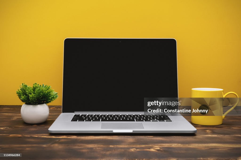 Laptop and Yellow Coffee Mug on Office Desk Against Yellow Background