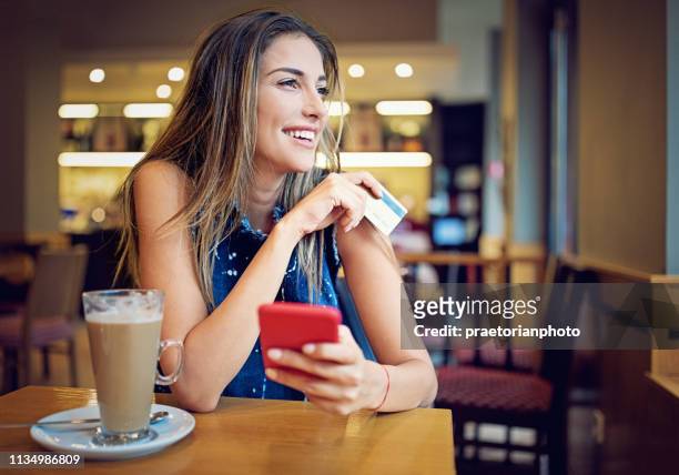 young girl is sitting in a cafe, and shopping online using her credit card - business girl stock pictures, royalty-free photos & images