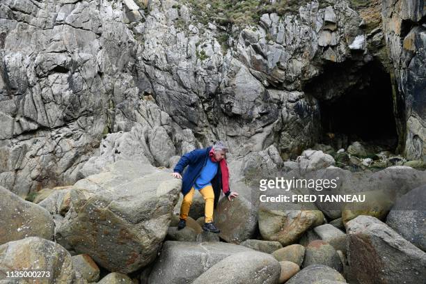 Voluntary of the French association Ar Viltansou climbs rocks in front of the entry of a partially submerged cave only accessible at low tide where a...