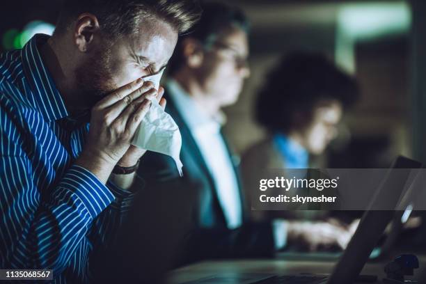 ill businessman blowing nose while working late in the office. - viral stock pictures, royalty-free photos & images