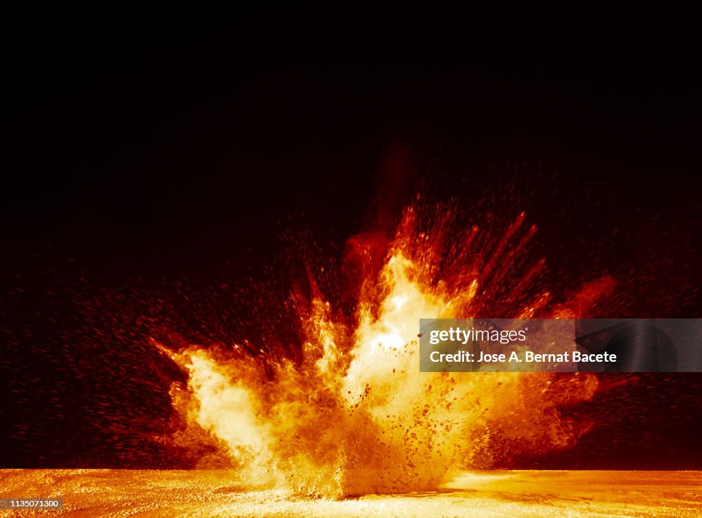 Explosion by an impact of a cloud of particles of powder and smoke of color yellow and orange on a black background.