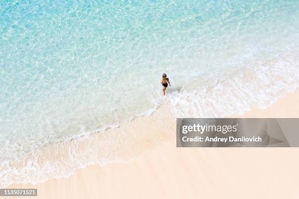 bali, young woman on the white sand beach beside the transparent turquoise sea. aerial drone shot. - white bay stock pictures, royalty-free photos & images