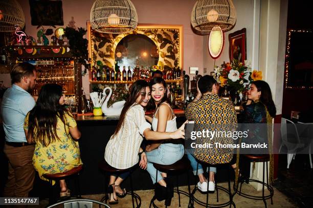 female friends taking selfie with smart phone while sitting at bar in night club - night out stock pictures, royalty-free photos & images