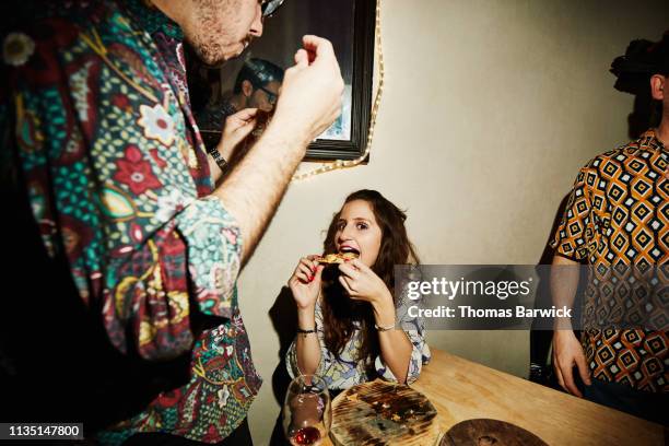 smiling woman taking bite of pizza during party with friends in night club - cuisine humour stock-fotos und bilder