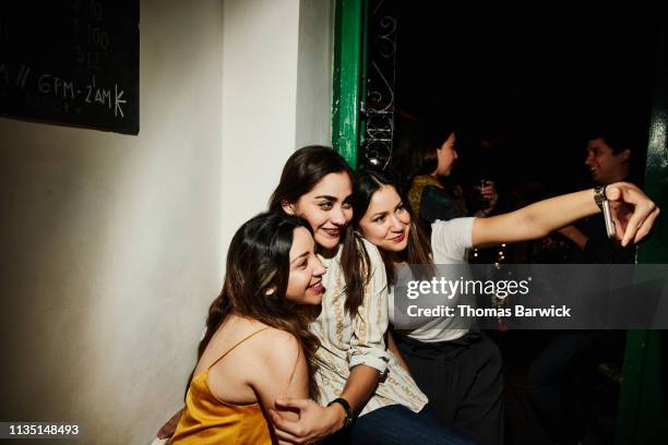 smiling female friends taking selfie with smart phone while hanging out in night club - millennials at party photos et images de collection