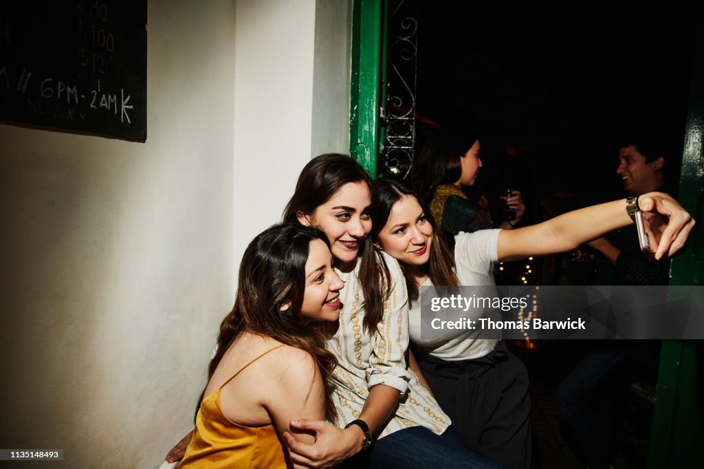 Smiling female friends taking selfie with smart phone while hanging out in night club