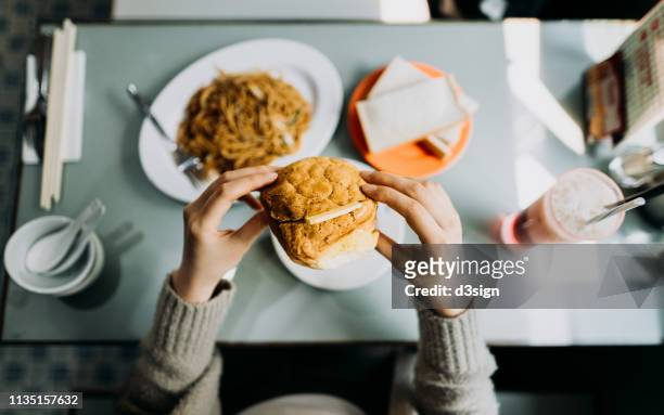 personal perspective of woman eating hong kong style local foods, sandwich, buttered pineapple bun, fried noodles and iced red bean drink in traditional restaurant - cafe culture stock-fotos und bilder