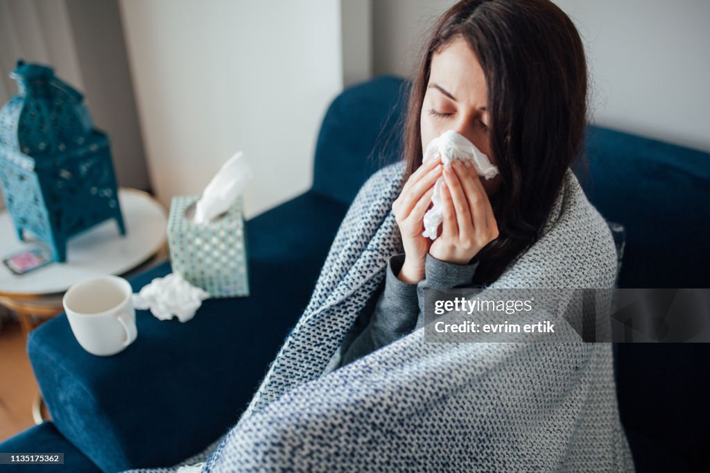 Sick woman blowing her nose, she covered with blanket