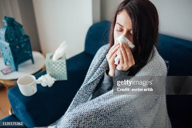 sick woman blowing her nose, she covered with blanket - tossir imagens e fotografias de stock