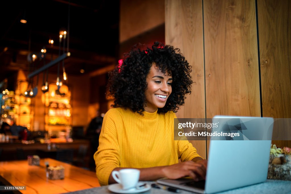 Donna sorridente che usa il laptop al bar.