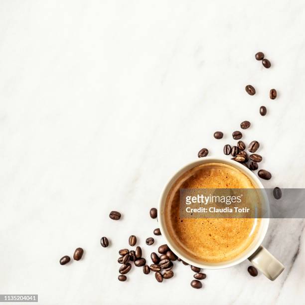 a cup of coffee and coffee beans on white, marble background - overhead view stock-fotos und bilder