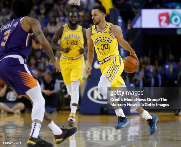 Golden State Warriors' Stephen Curry dribbles behind his back against Phoenix Suns' Kelly Oubre Jr. In the first quarter at Oracle Arena in Oakland,...