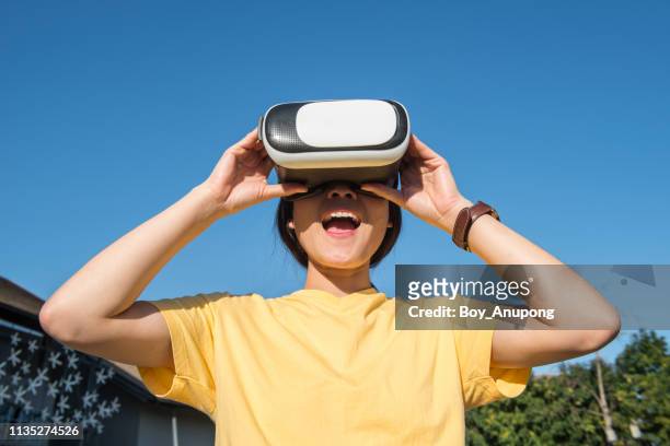 portrait of young asian woman wearing virtual reality goggles and exciting the vr simulation experience. - casques réalité virtuelle photos et images de collection